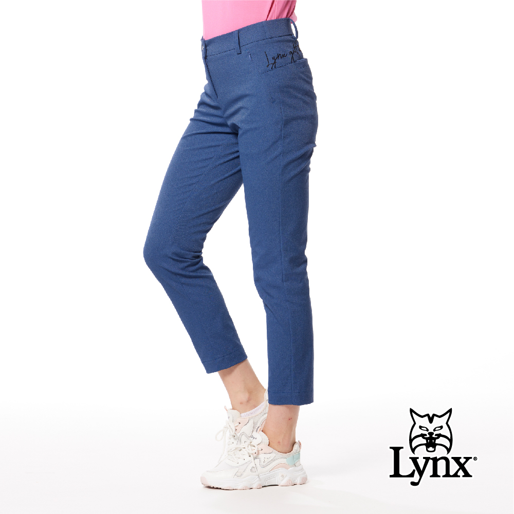 【Lynx Golf】女款日本進口布料抗皺彈性舒適丹寧風格織帶剪接設計草寫繡花造型窄管九分褲-深藍牛仔色